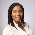 Ivy Gray, a Black woman wearing a very light pink blouse, poses for a headshot.