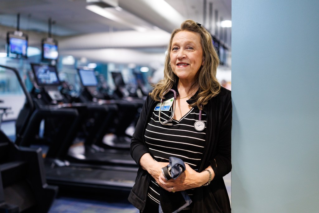 A woman leans on a wall in a gym with exercise machines