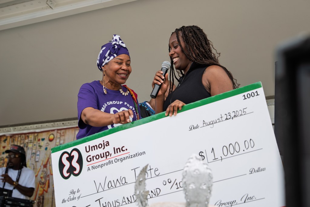 A woman receives a large check from another woman holding a micrphone