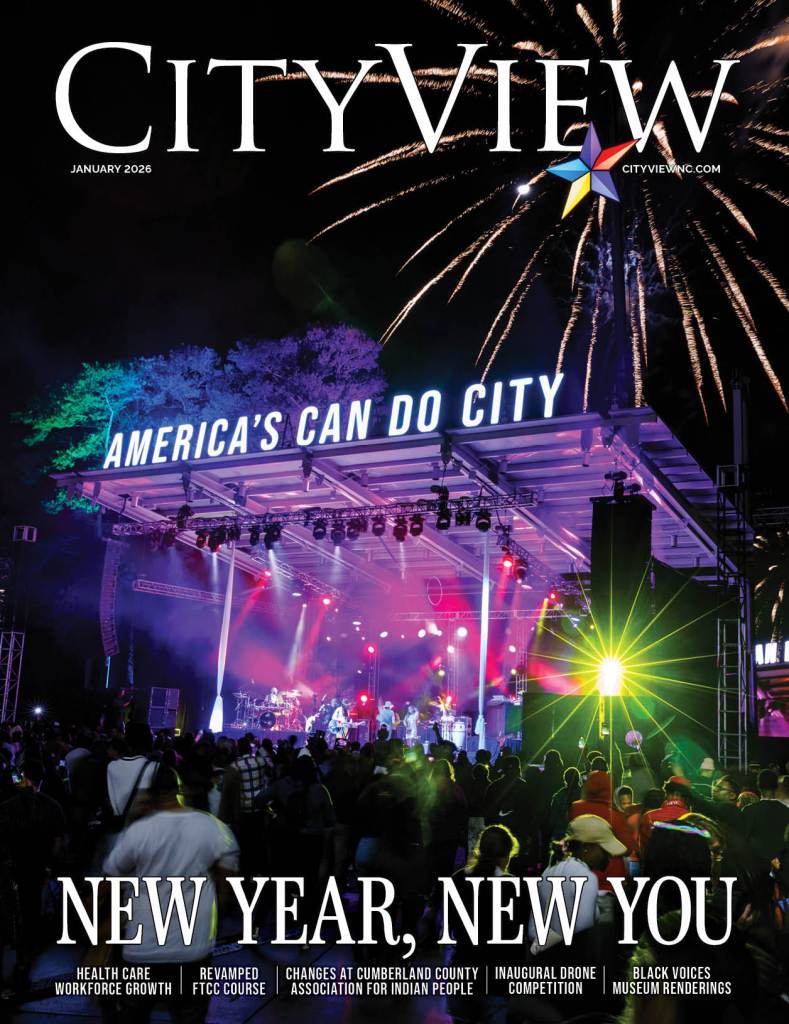 A crowd watching a lit stage at night with a band playing and fireworks in the background